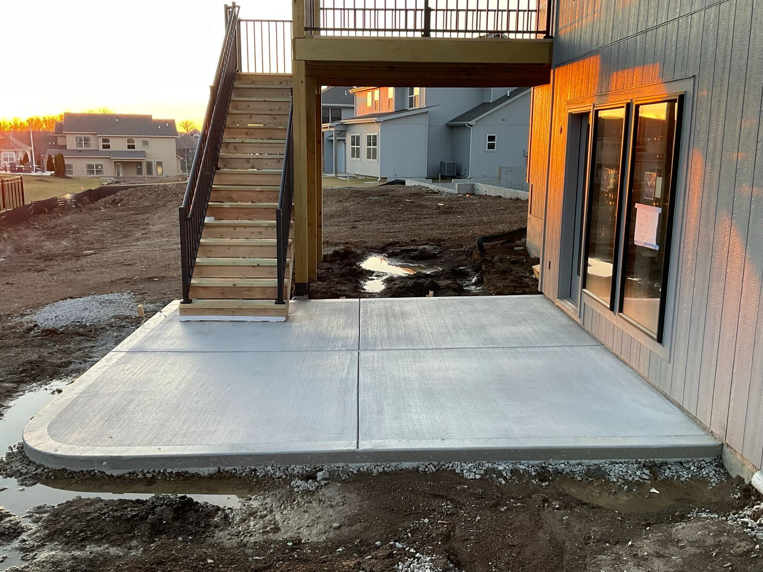 Finished concrete patio with deck stairs descending to it at golden hour
