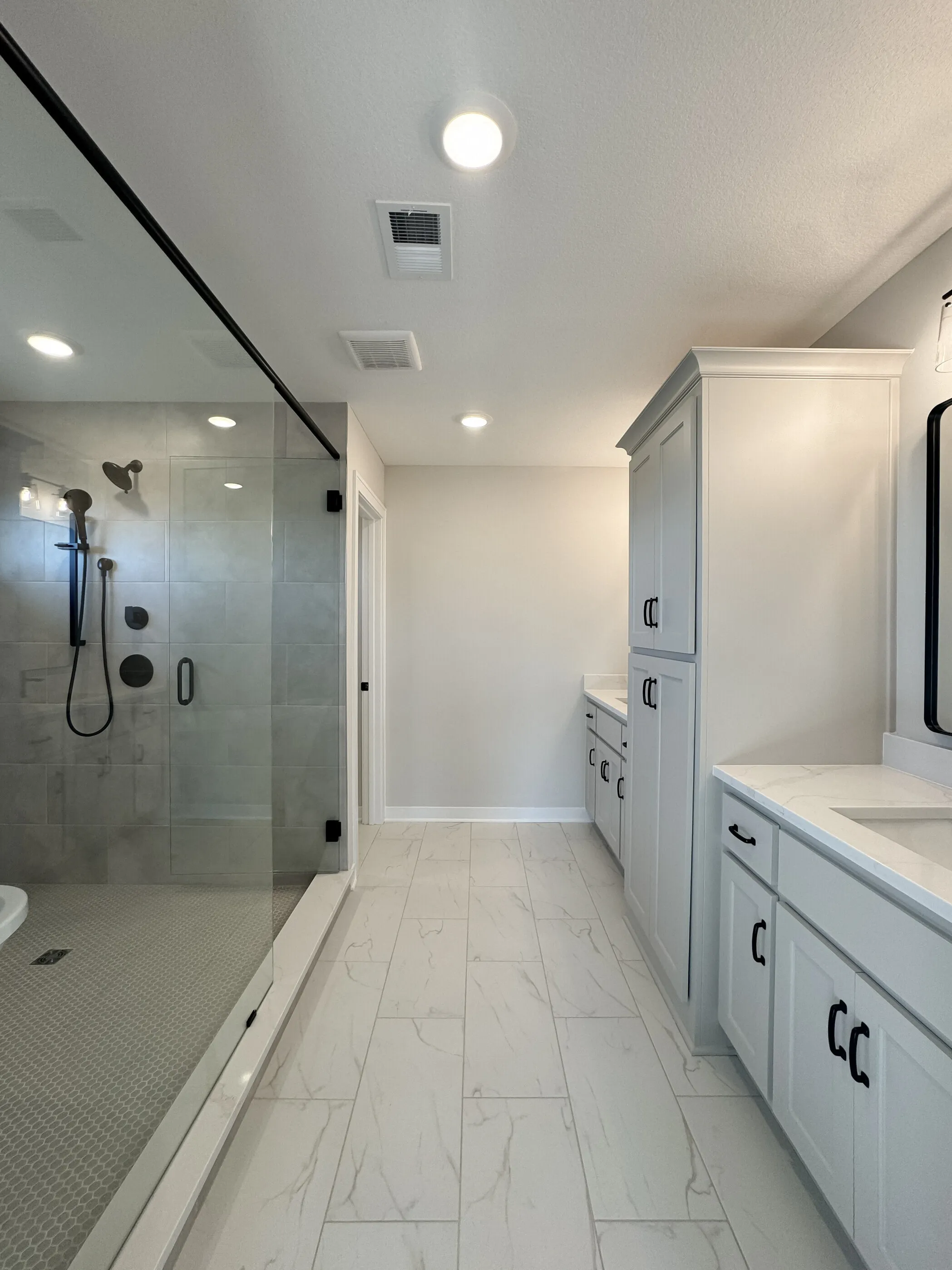 Primary bath with frameless glass shower, marble-look tile floor, and shaker double vanity