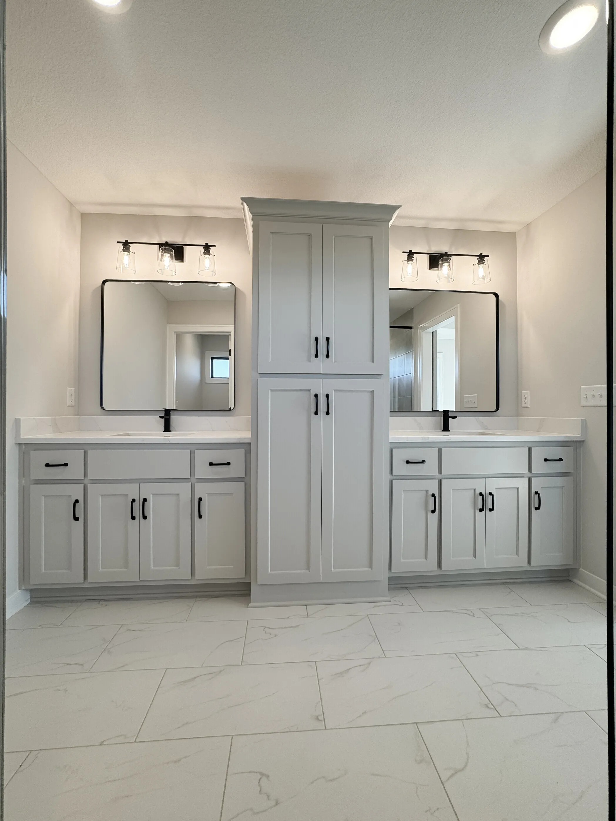 His-and-hers double vanity with center tower cabinet and marble tile floor